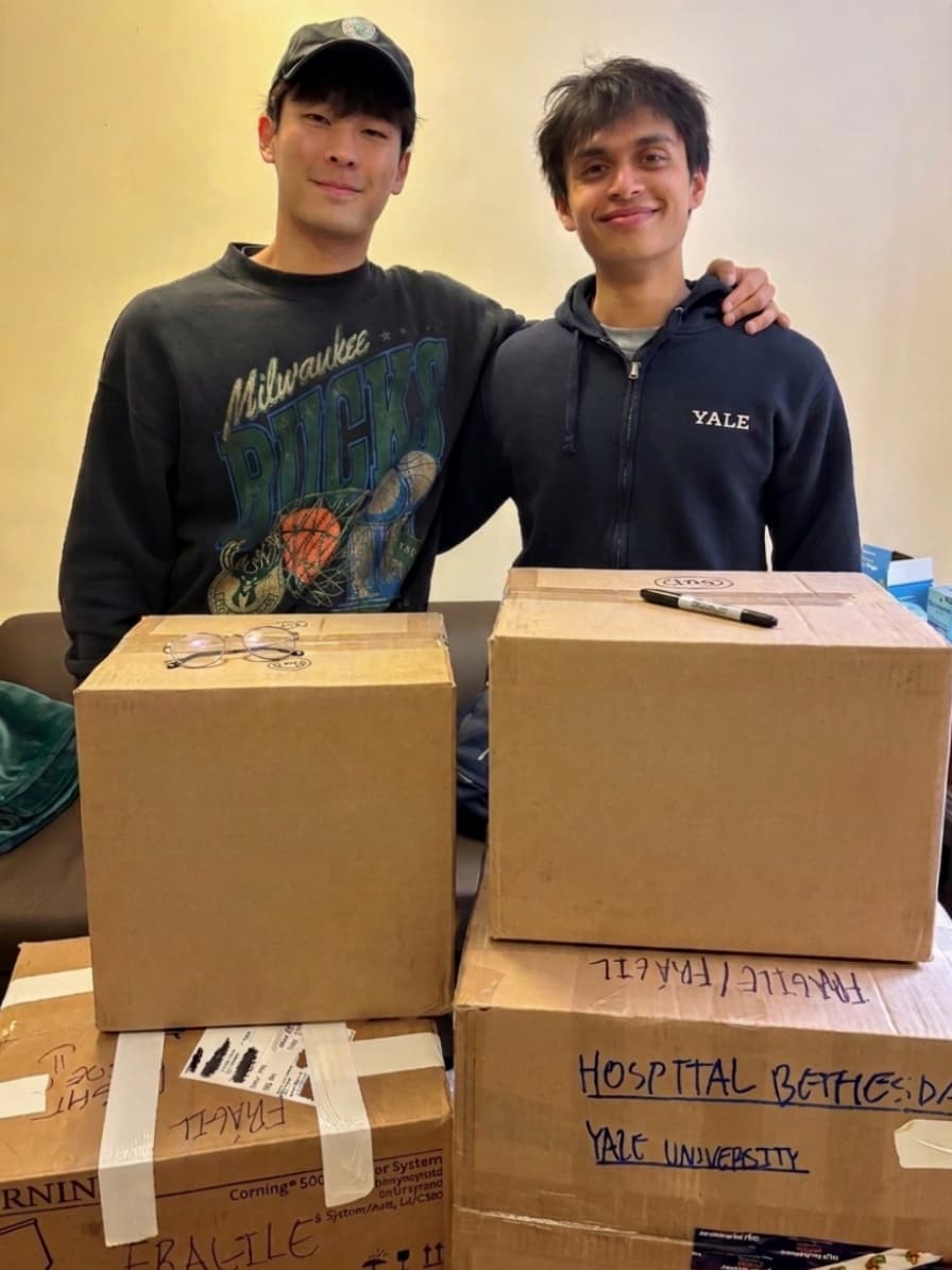 Josh and Sebastian standing behind packed boxes for Hospital Bethesda at Yale University